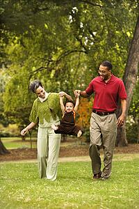 Mother and father swinging toddler holding his hands in park