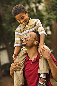 Father carrying his son on his shoulders smiling and looking at each other