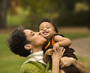 Head and shoulder portrait of woman holding and kissing boy as he smiles.