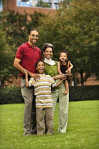 Family of four standing in park smiing.