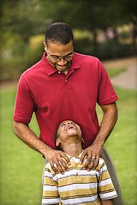 Father standing behind son with hands on his shoulders as boy smiles