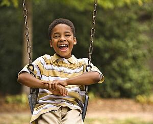 Happy smiling boy on swing in park playground
