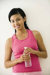 Portrait of smiling young woman standing in fitness clothes holding bottle of water
