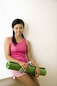 Portrait of smiling young Asian woman holding yoga mat.