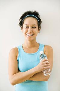 Young woman in exercise clothes holding bottle of water smiling.