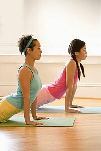 Two young women on yoga mats doing upward cobra pose