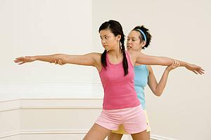 Young woman helping another young woman with positioning on her yoga pose.