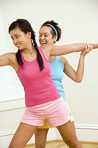 Young woman helping another young woman with positioning on her yoga pose