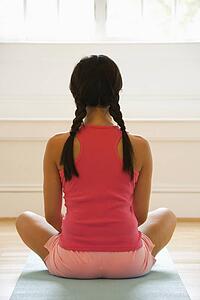 Rear view of young woman sitting on mat with legs crossed in yoga pose.