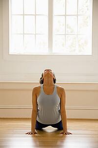 Young woman doing yoga cobra pose on wooden floor indoors by sunlit window