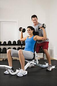 Man assisting woman at gym with hand weights smiling