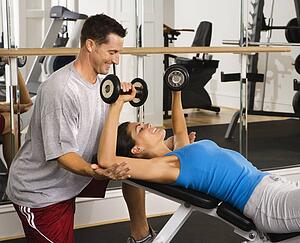 Man assisting woman at gym with hand weights smiling
