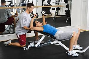 Man assisting woman at gym with hand weights and smiling