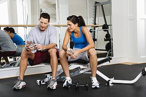 Man and woman sitting on exercise machine talking holding water bottles