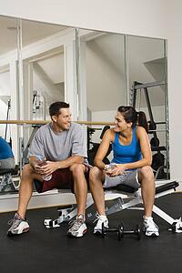 Man and woman sitting on exercise machine talking holding water bottles.