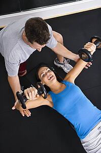 Man assisting woman lifting weights at gym