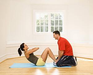 Man holding woman's feet down as she does sit up exercises