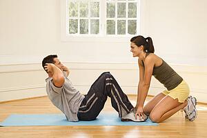 Woman holding man's feet down as he does sit up exercises