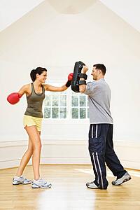 Woman wearing boxing gloves hitting training mitts man is holding