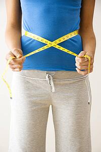 Woman standing pulling measuring tape around waist