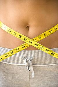 Woman pulling measuring tape around bare waist.