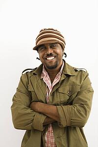 African-American mid-adult man wearing hat and smiling at viewer with arms crossed.