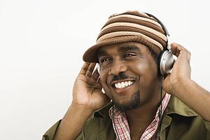 African-American mid-adult man wearing knit hat and listening to headphones smiling.