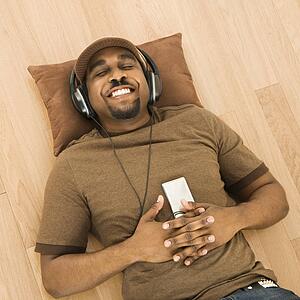 Man wearing headphones and listening to mp3 player while lying on back on floor