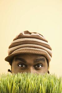 Man wearing knit hat with brim peeking from behind grass
