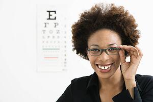 Woman with afro wearing eyeglasses with medical eye chart in background