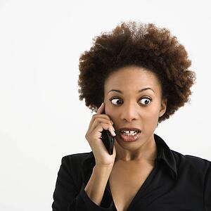 Woman talking on cellphone looking shocked against white background.