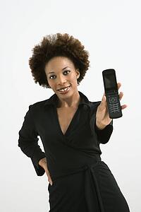 Woman holding cellphone out to view standing against white background.