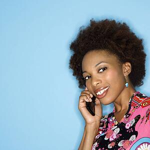 Woman with afro wearing vintage print fabric smiling holding cellphone