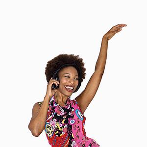 Woman with afro wearing vintage print fabric and listening to headphones smiling and dancing
