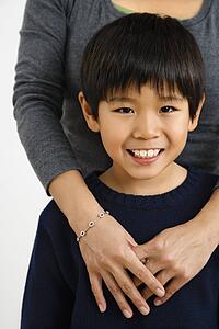 Boy smiling with mother standing behind with arms around him