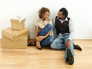 Portrait of smiling happy young couple sitting on floor of home with moving boxes