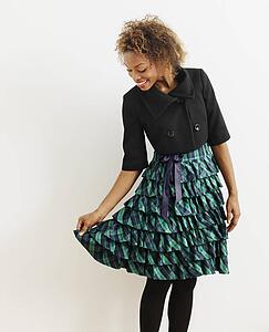Portrait of pretty young woman in dress holding it out to side smiling.