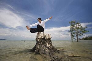 A man balancing on a tree stump on a beach in Koh Lanta, Thailand