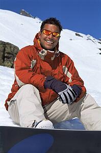 Snowboarder sitting on hill with board smiling (selective focus)