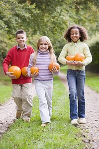 Three young friends walking on path with pumpkins smiling