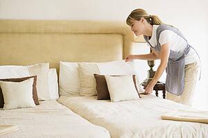 Maid making bed in hotel room smiling