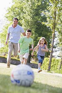 Man and two young children outdoors playing soccer and having fun