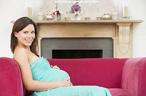 Pregnant woman sitting in living room smiling