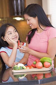 Mother Offering Daughter A Piece Of Freshly Chopped Pepper