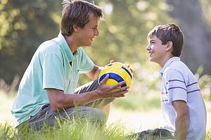 Man and young boy outdoors with soccer ball smiling