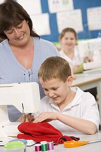 Male student using sewing machine with teacher