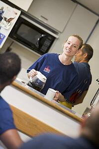 Four firefighters in break room with one getting coffee (selective focus)