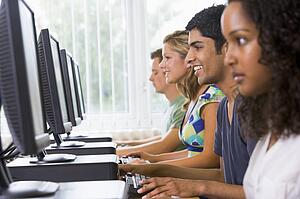 Four people sitting at computer terminals (selective focus/high key)