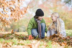 Two young children outdoors in park playing in leaves and smiling (selective focus)