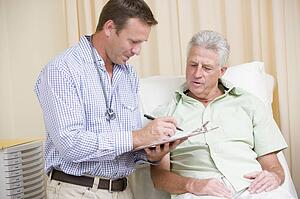 Doctor writing on clipboard while giving man checkup in exam room